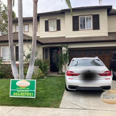 House with a plumbing service sign on the lawn and a car parked in the driveway.