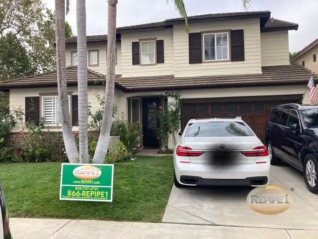 House with a plumbing service sign on the lawn and a car parked in the driveway.
