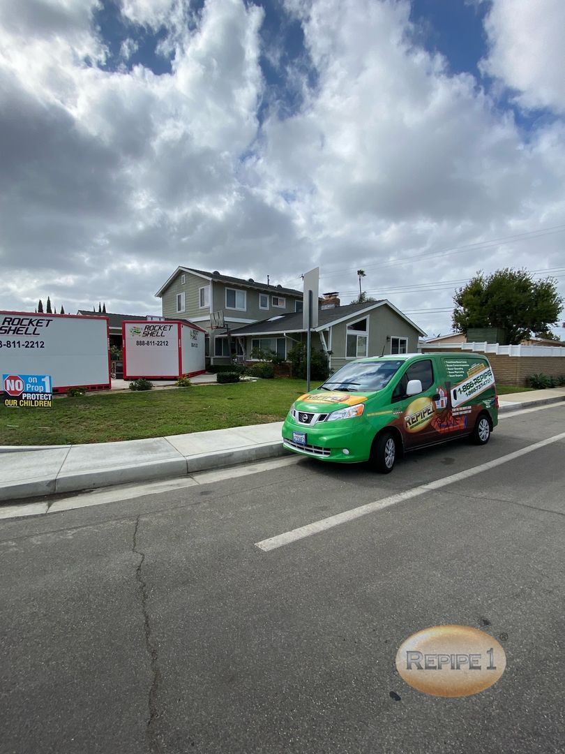 Repipe1 service van parked in front of a house with Rocket Shell containers nearby.