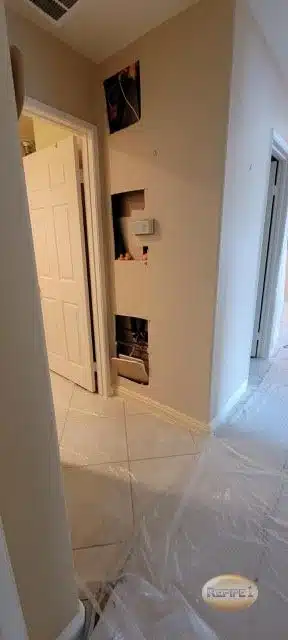 Hallway with wall cutouts showing exposed plumbing