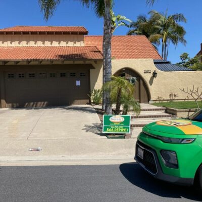 House with a sign for a plumbing service and a green service vehicle parked in front.