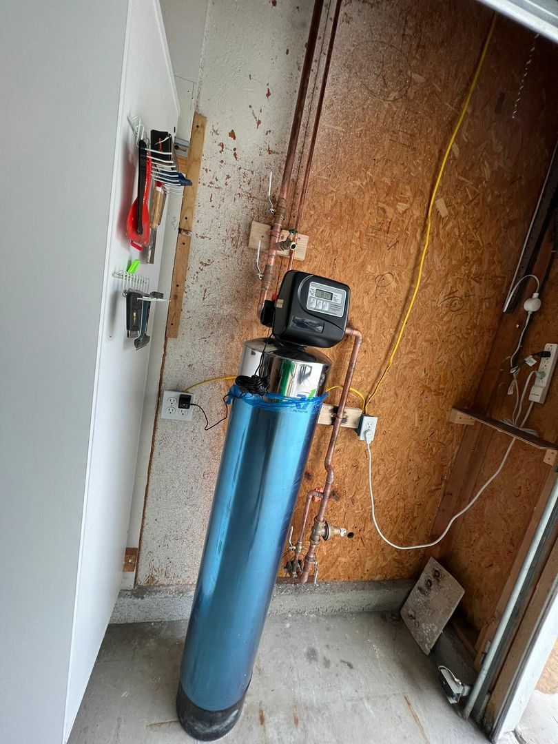Installed water softener system in a garage with visible plumbing pipes and electrical connections, highlighting recent home improvement efforts.