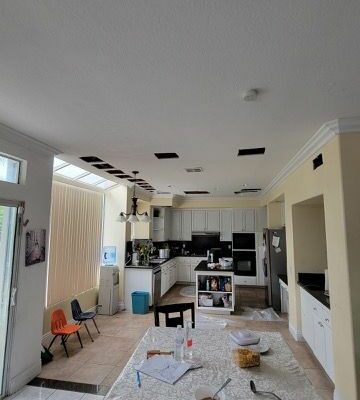 Kitchen and dining area with ceiling cutouts showing renovation work, table with scattered items in the foreground.