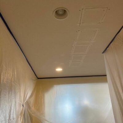 Ceiling with patched holes and plastic sheeting covering the walls, indicating renovation work.