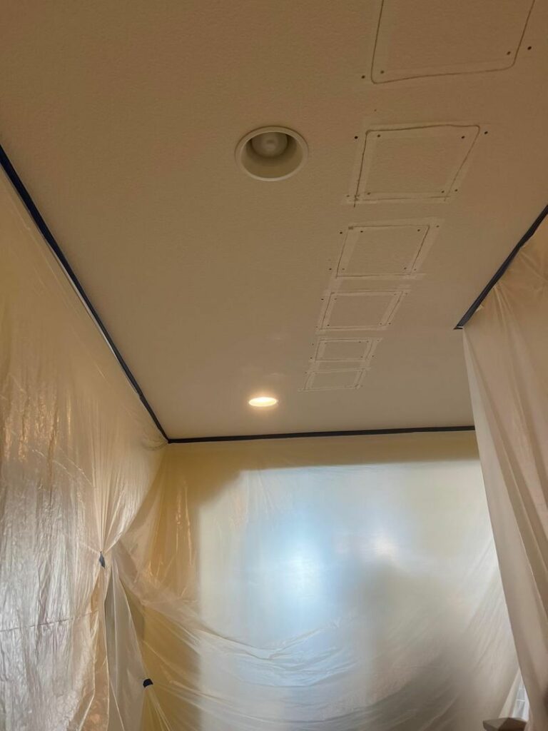 Ceiling with patched holes and plastic sheeting covering the walls, indicating renovation work.