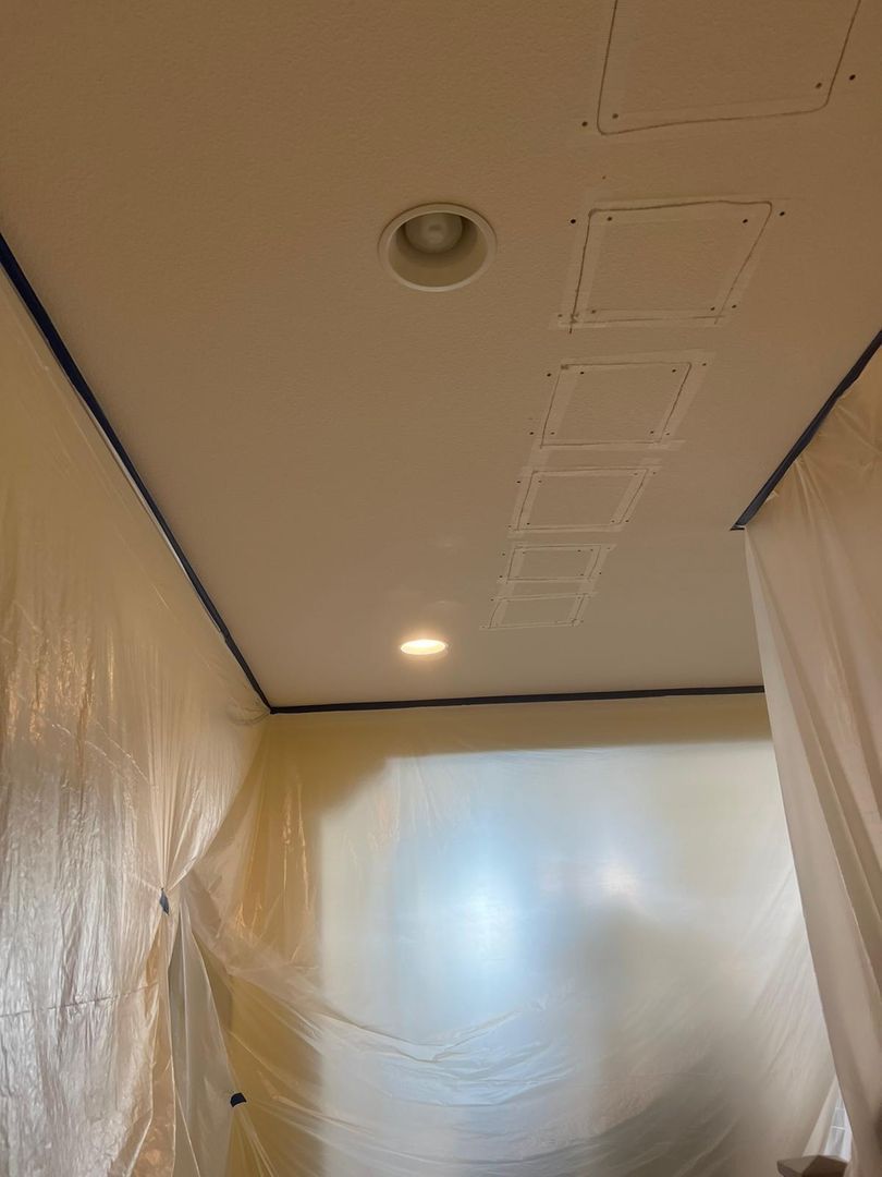 Ceiling with patched holes and plastic sheeting covering the walls, indicating renovation work.