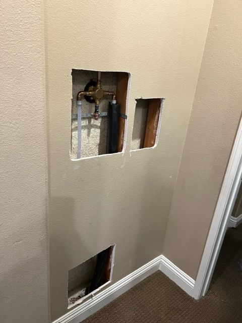 Wall with cutouts showing exposed plumbing pipes, indicating repair work.